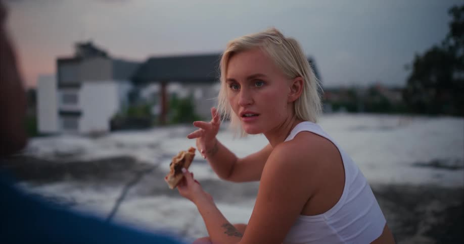 A blonde woman is sitting and talking to someone in front of her while holding a food