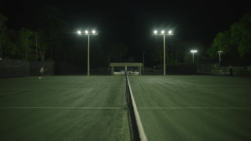 Two people playing tennis on a court at night