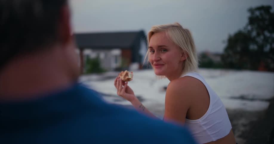 A man and a woman eating pizza have a conversation outdoors
