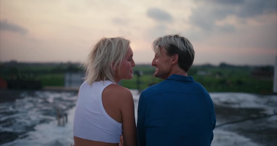 A man and a woman sit together and kiss while outdoors