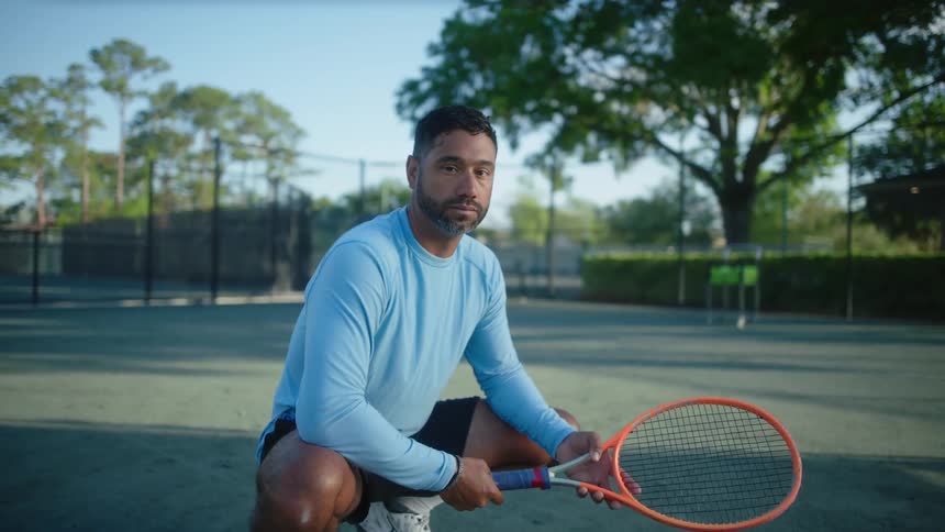 A man is crouched holding a tennis racket and staring straight ahead