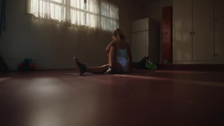 A woman sitting in the floor of a dimly lit room stretches