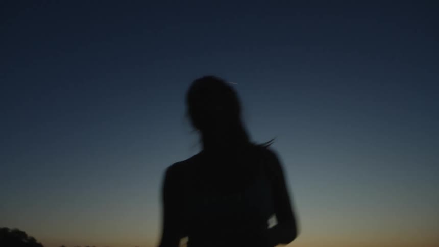 Silhouette of a woman serving a tennis ball under a twilight sky