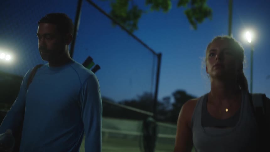 Man and woman walking side by side at night next to a tennis court