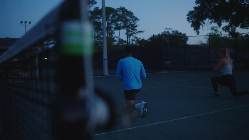 Man and woman doing squats on a tennis court
