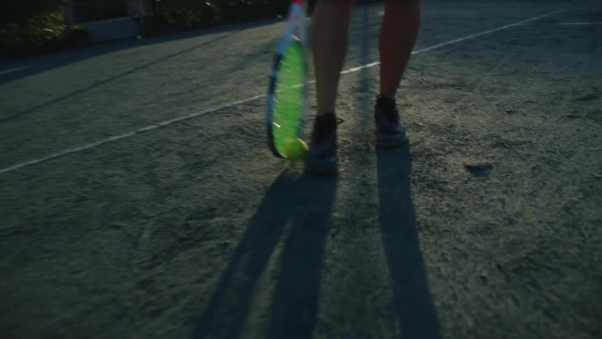 Woman catching a tennis ball that is rolling on the court with her racket