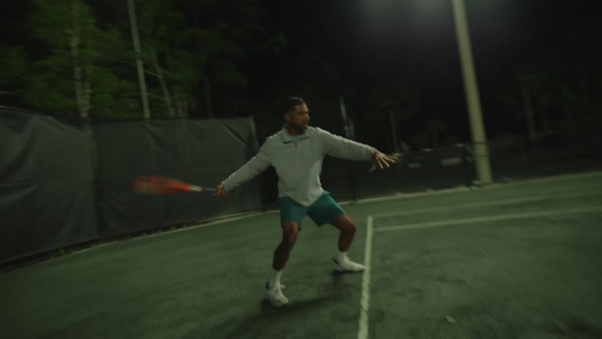 Man playing tennis on a court in the open sky at night