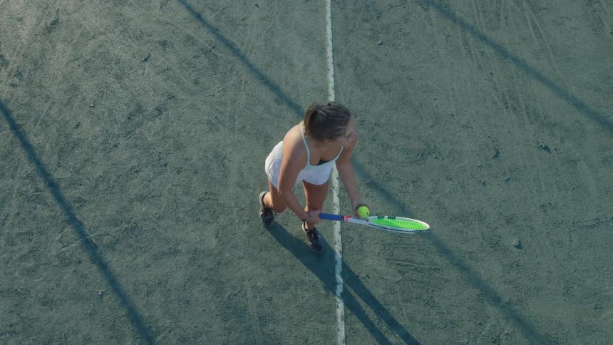 A female tennis player stands on a court throwing a ball in the air ready to serve