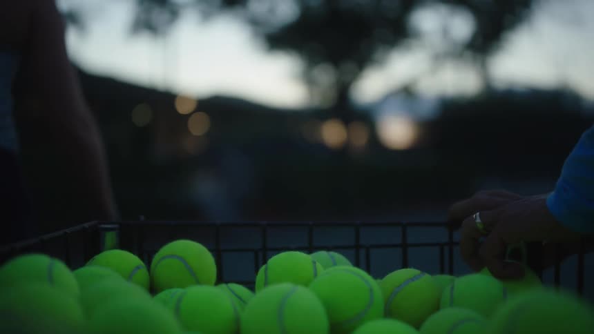 Players pull a basket cart full of tennis balls to practice with