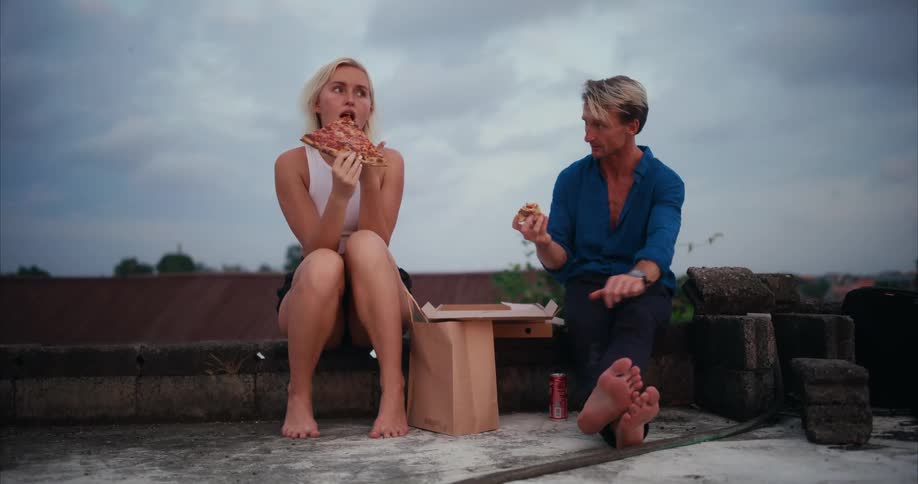 Man and woman sitting outdoors talking and eating pizza