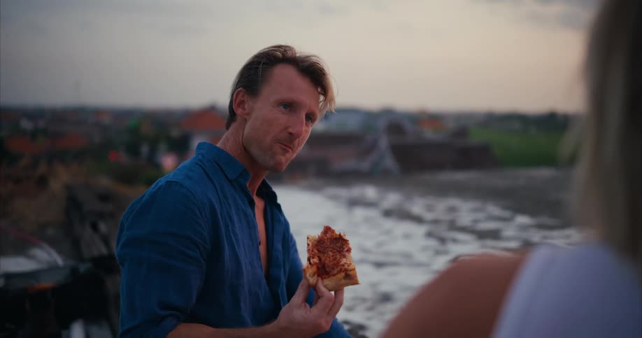 A couple eating pizza in the roof of a building at evening