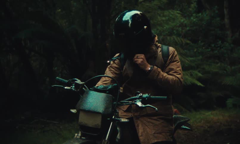A young man dons a helmet and starts a motorcycle in a forest