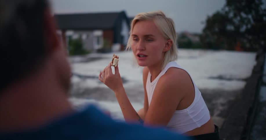 A blonde woman talking to someone in front of her while eating a dessert