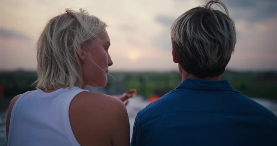 A young couple eating pizza outdoors looking at the sunset