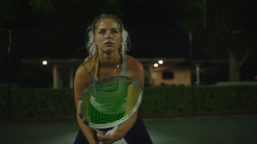 A woman is playing tennis at night