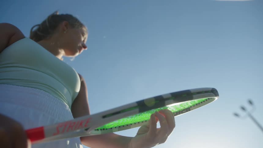 A woman is holding a racket and testing the string tension