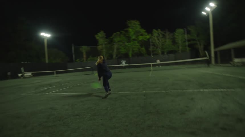 A woman in black is playing tennis on a court against another person and is competitive