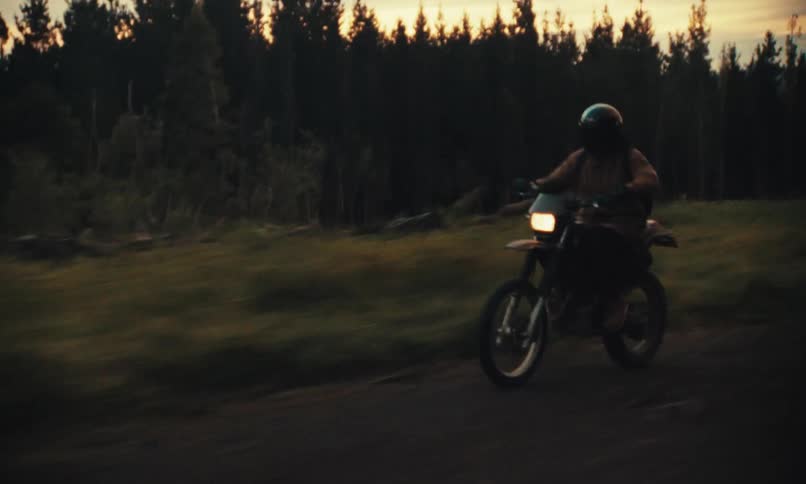 Person riding a motorcycle on a dirt road with trees around