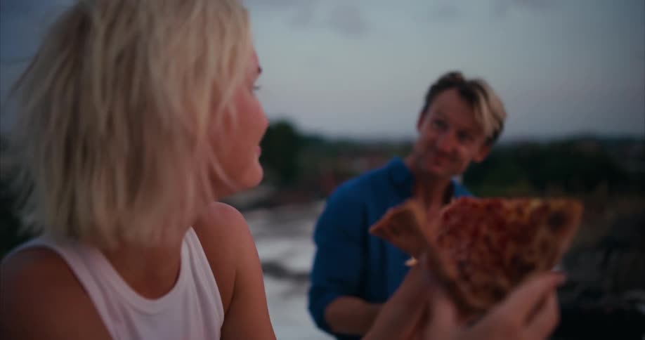 Man and woman sitting and talking in an openair place eating pizza