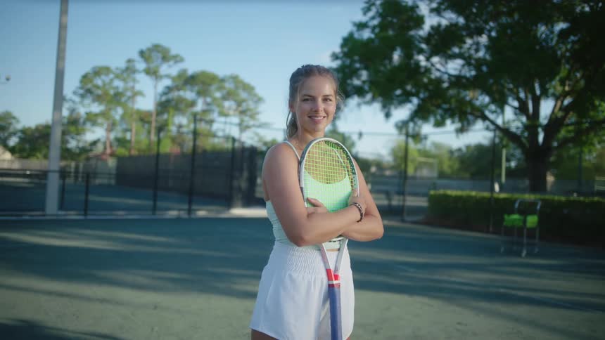 A young teenage tennis player smiles while standing on a court