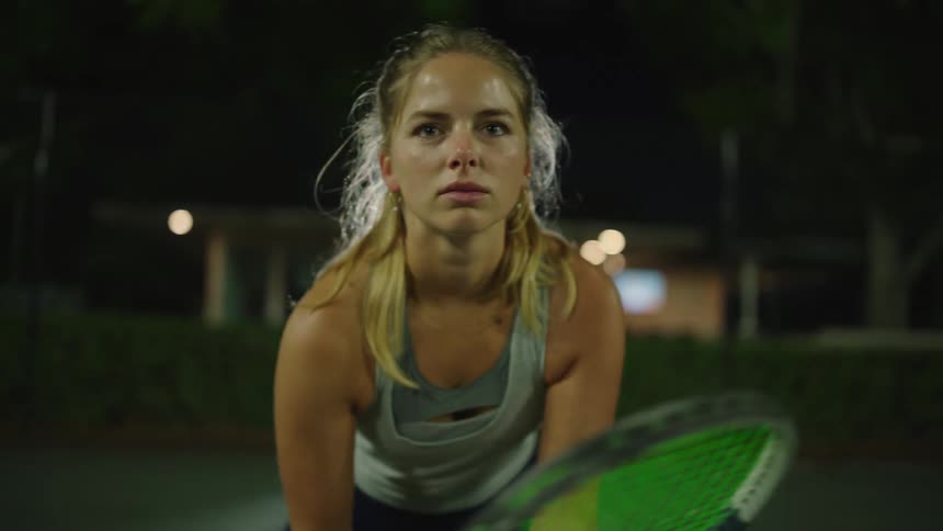 Concentrated woman holding racket on a tennis court at night