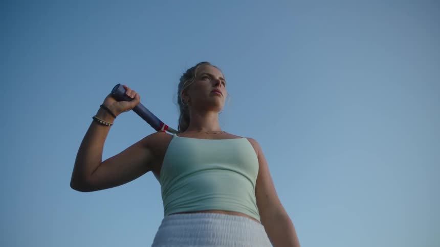 A tennis player holding a racket over her shoulder under a clear blue sky