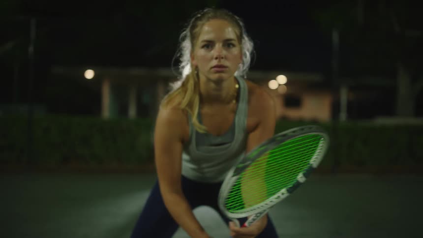 Concentrated woman holding a racket while standing on a tennis court at night