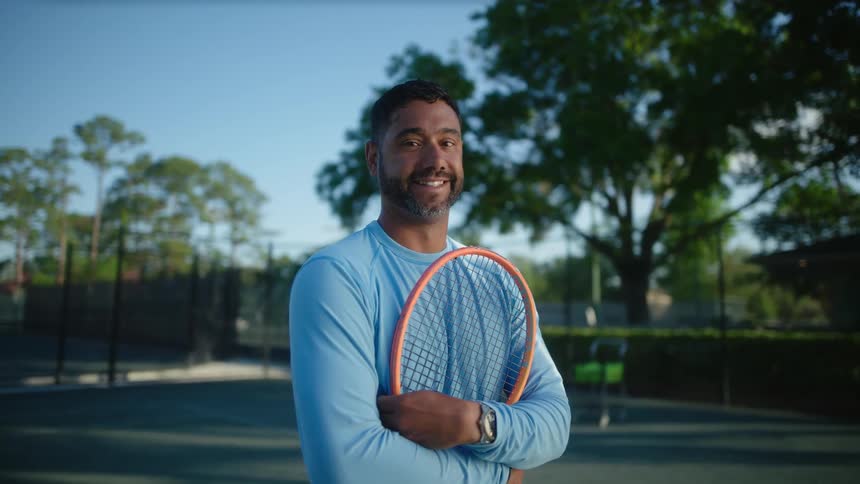 Smiling man posing with a racket on a tennis court