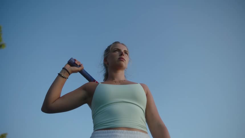 A tennis player holding a racket over her shoulder under a clear blue sky