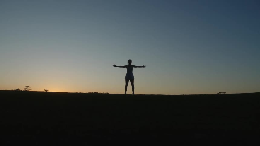 A silhouette of a person standing with arms open on a dark morning with a bright sky