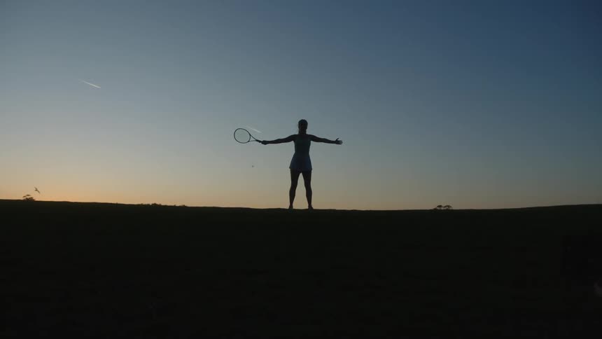 Silhouette of a woman holding a racket with open arms against a late afternoon sky