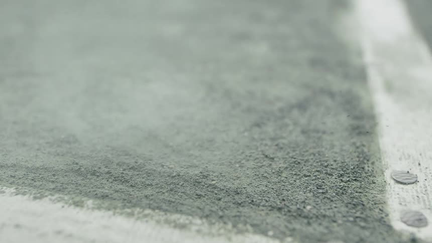 A tennis ball bounces on the ground of a court kicking up dust