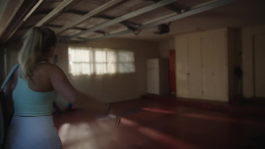 A female tennis player opens a garage door to a house and walks inside