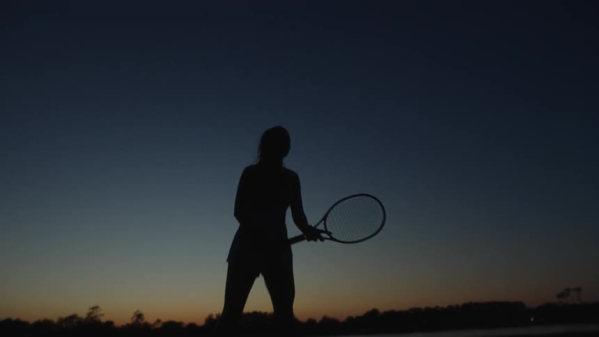 Silhouette of a woman jumping and playing tennis at dusk