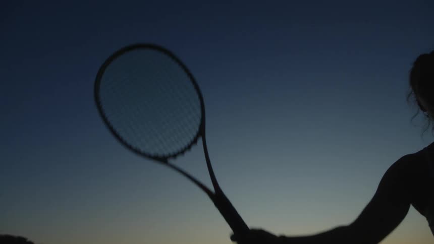 Silhouette of a tennis player holding a racket over her shoulder under twilight sky