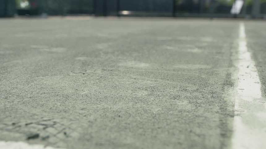 Green tennis ball hitting the ground on a court during the day