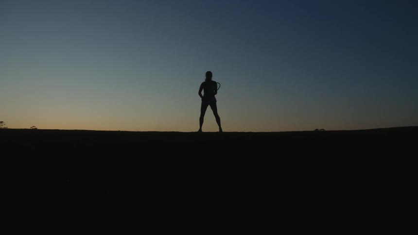 Silhouette of a woman against a dawn sky holding a racket and making tennis moves