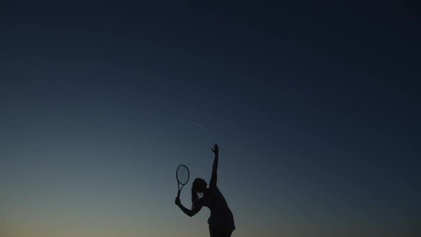 Silhouette of a woman in shooting position holding a tennis racket against a blue sky