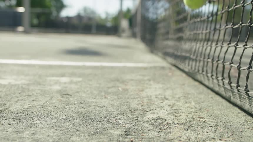 Tennis ball bouncing and kicking up dust, then brushing against the net on tennis court.
