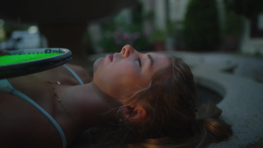 A woman resting over a bench with a tennis racket on her chest at morning