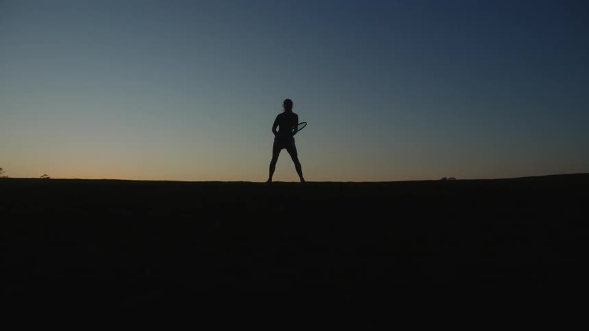 A woman is swinging her tennis racquet at sunrise