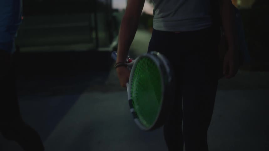 Two tennis players walk on a sidewalk near tennis courts