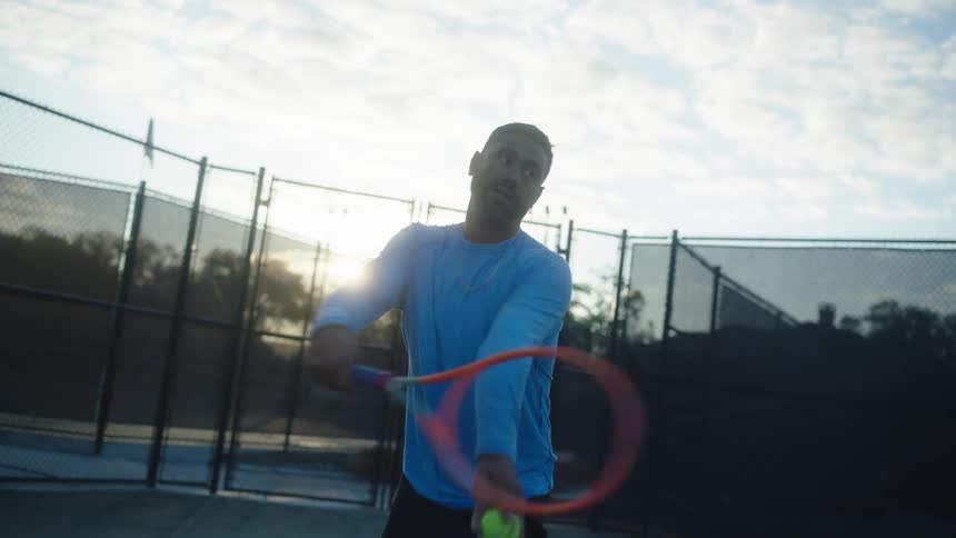 A male tennis player tosses the ball up and serves