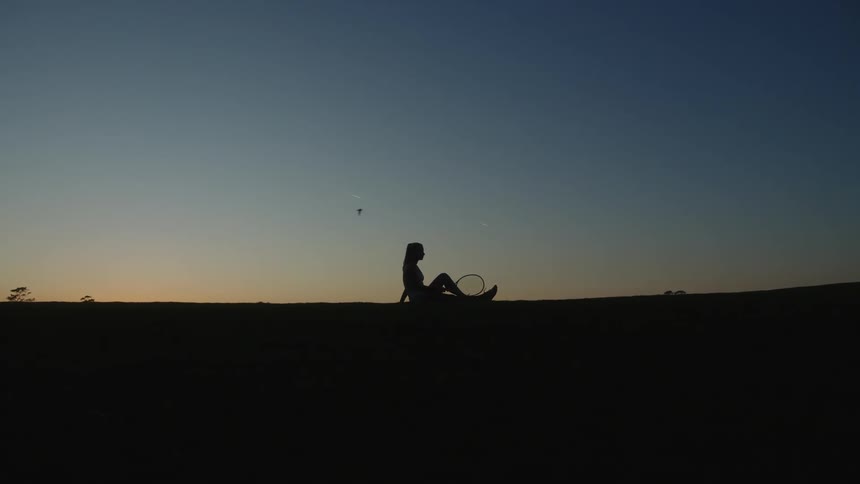 Silhouette of a tennis player sitting on the ground under a twilight sky