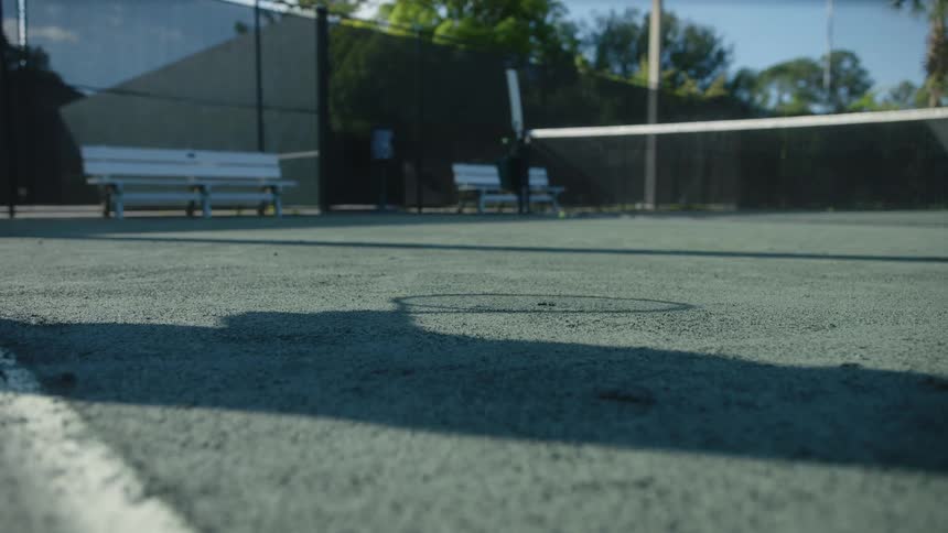 Shadow of a tennis player and racket with a ball bouncing on the court