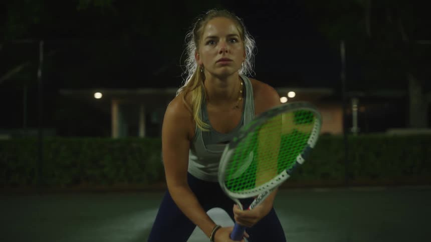Woman holding a tennis racket on an outdoor court at night