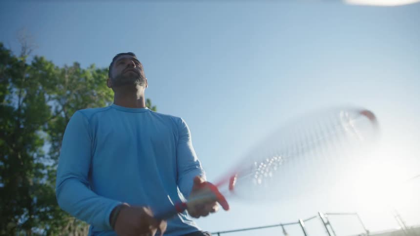 A man holding a tennis racket ready to play on a bright sunny day