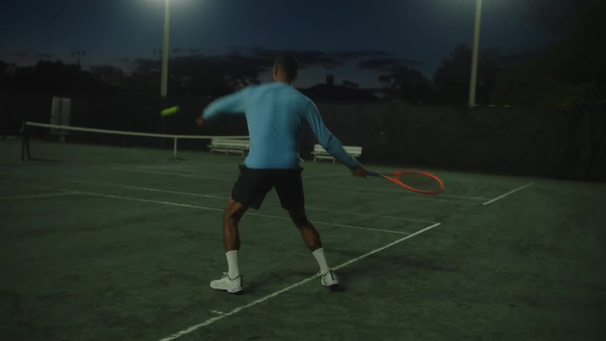Man on a court at night playing tennis