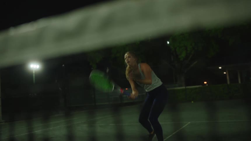 Woman playing tennis on a court at night