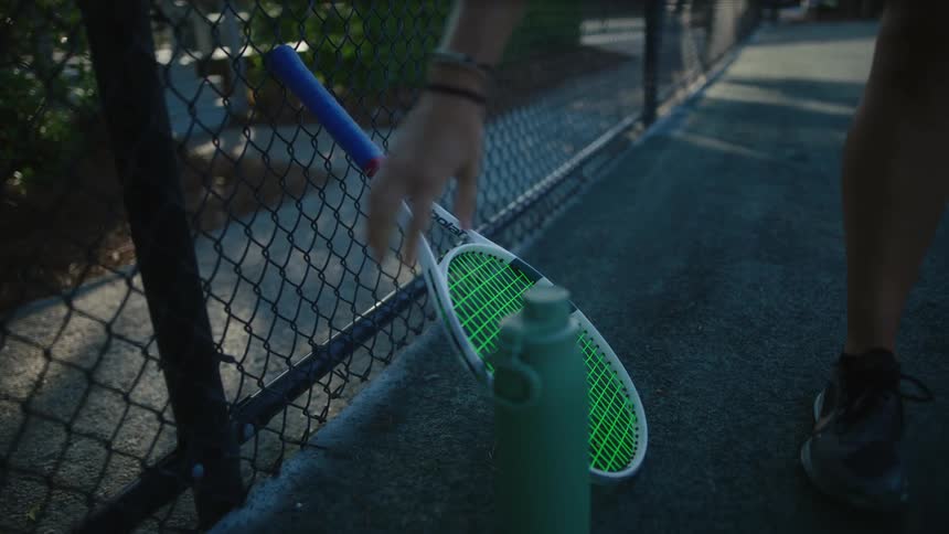 Female tennis player on court puts down water bottle and picks up tennis racket